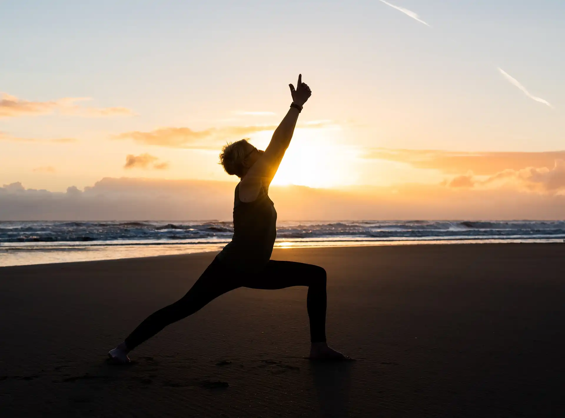 A woman in silhouette doing warrior yoga pose on the beach.