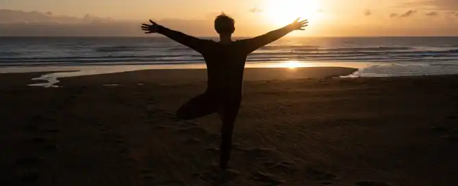 A women in silhouette on the beach doing yoga