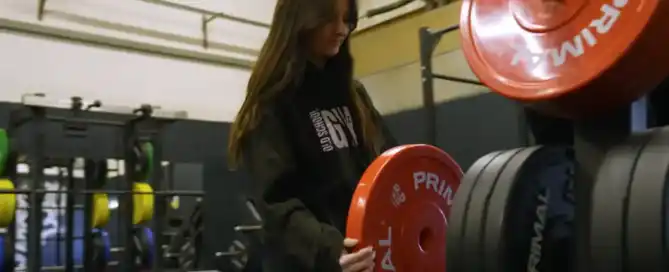 A women lifts a read weight onto equipment in a gym.