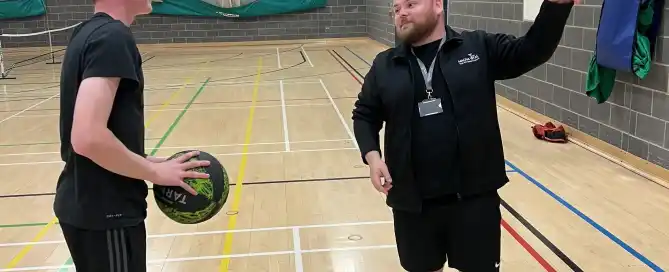 A man talks to a teenage boy on a basketball court.