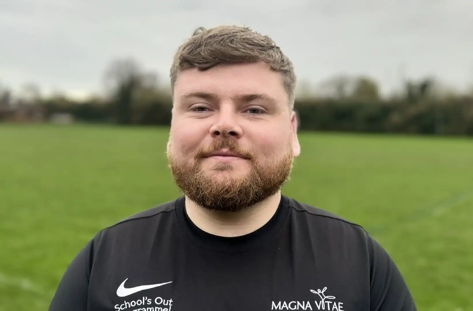 A close up headshot of a man, with a field in the background.
