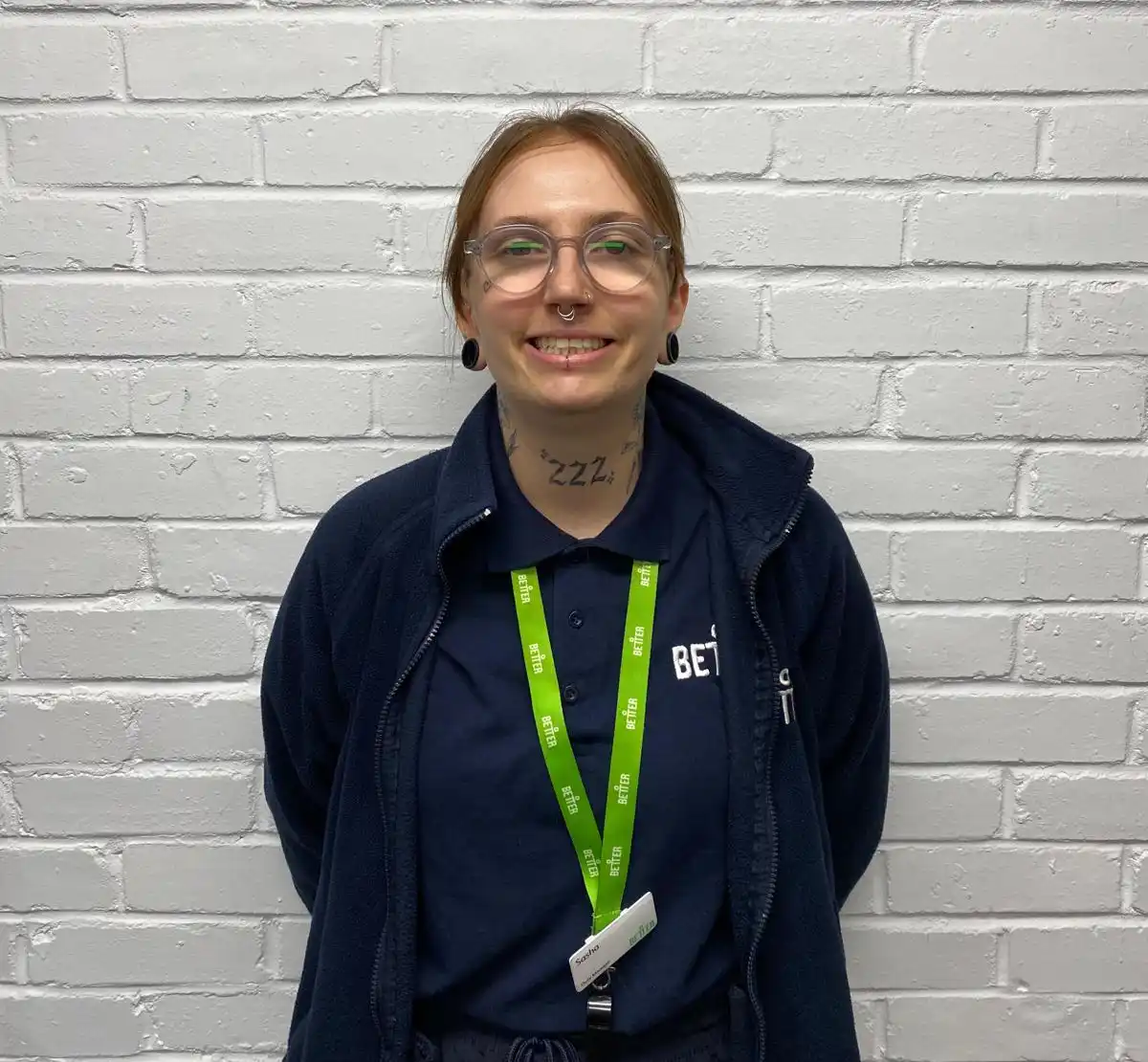 A lady with a GLL hoody and lanyard poses for a photos against a white brick wall