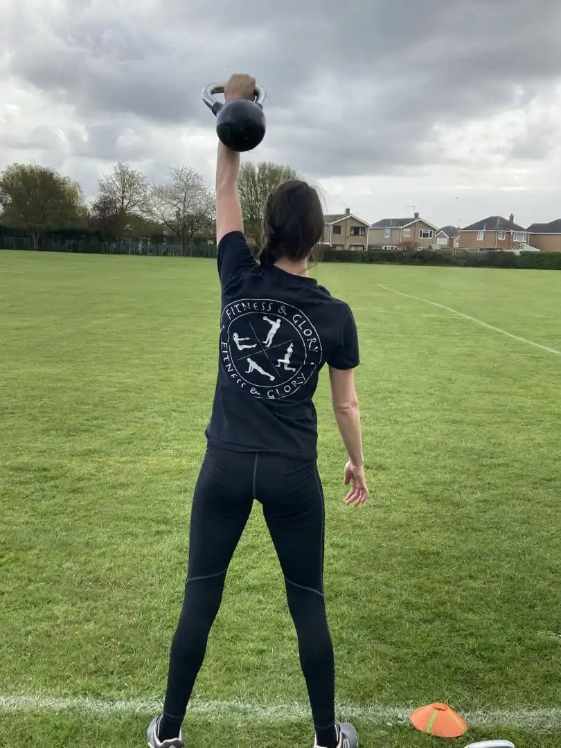A women seen from behind lifts a kettle bell above her head.