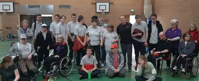 A group of people some with disabilities, pose for photo in a sports hall.